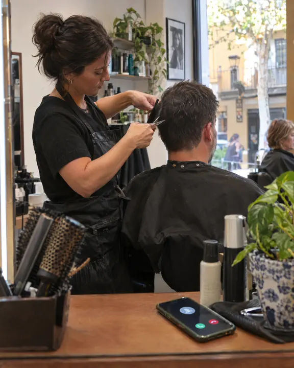 Una peluquera corta el pelo a un cliente mientras el móvil suena en el mostrador