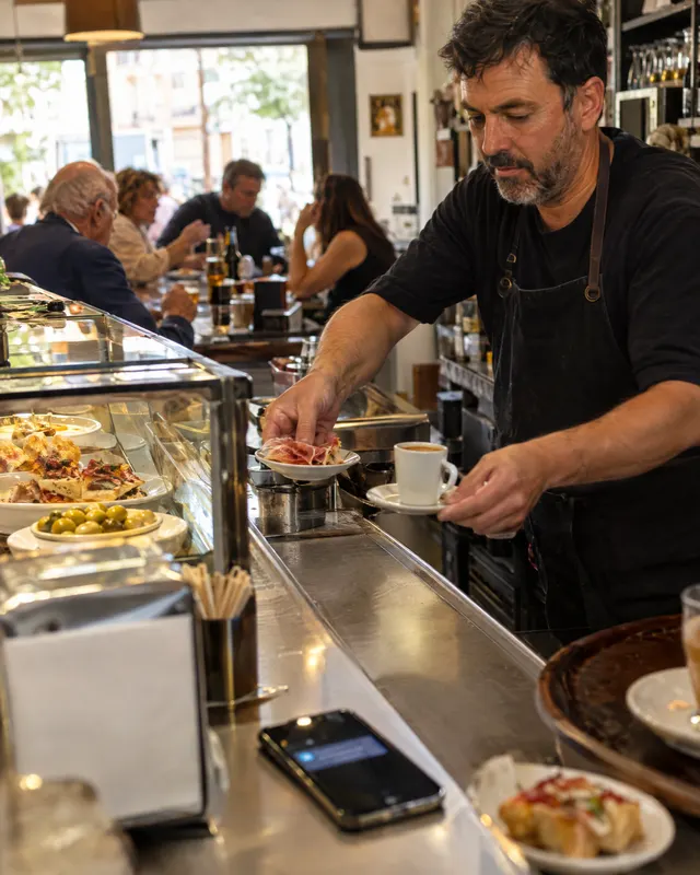 El dueño de un bar sirve cafés y tapas mientras el móvil se ilumina en la barra